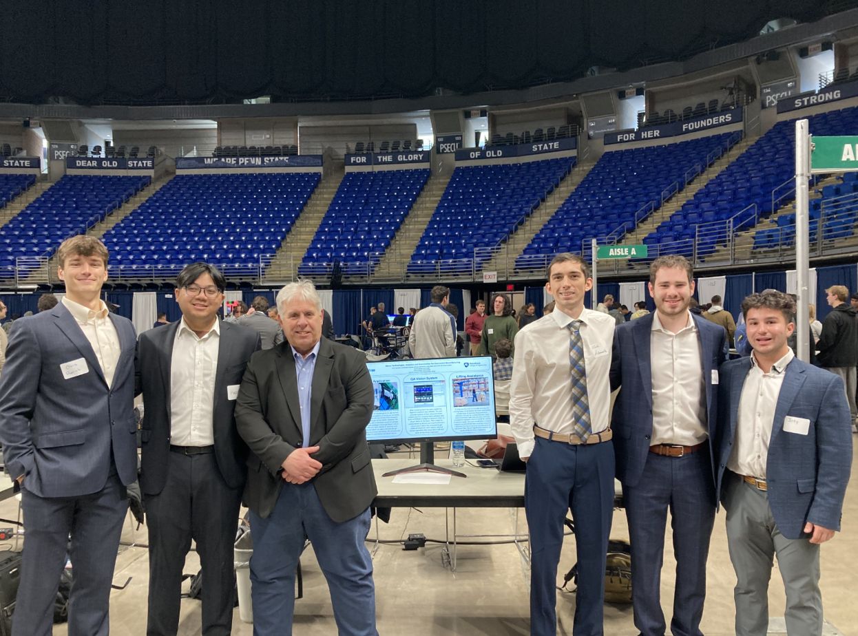 A group of men stand next to a table with a computer monitor